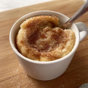 Delicious cinnamon roll mug cake topped with icing in a white mug.